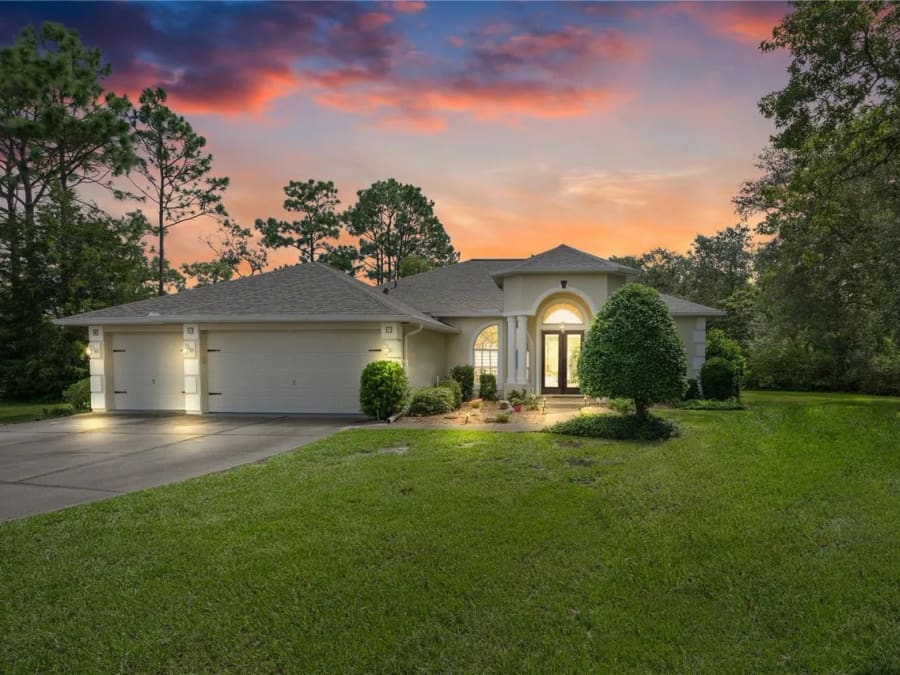 Twilight view of the single-story home at 1 Colubrina Ct, Homosassa, with a lit entry and three-car garage